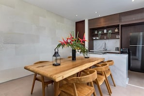 A modern kitchen with a wooden dining table, chairs, and a refrigerator. - Blanc Haven Canggu by Kerta Living (Badung)