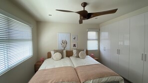 Ein Schlafzimmer mit Bett, Deckenventilator, Nachttisch, Kleiderschrank und Wandbild.