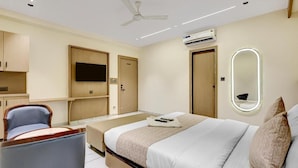 Habitación de hotel con cama, una silla, televisor, equipo de aire acondicionado y ventilador de techo.