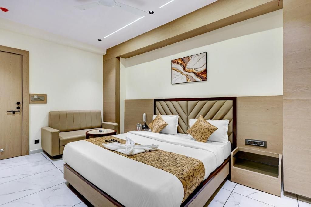 A hotel room with a large bed, a sofa, a bedside table, and a wall-mounted artwork.