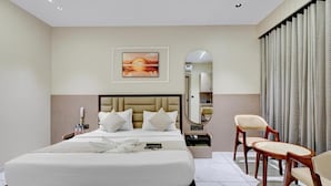 Habitación de hotel con una cama grande, una mesita de noche, una silla, un espejo y un cuadro en la pared.