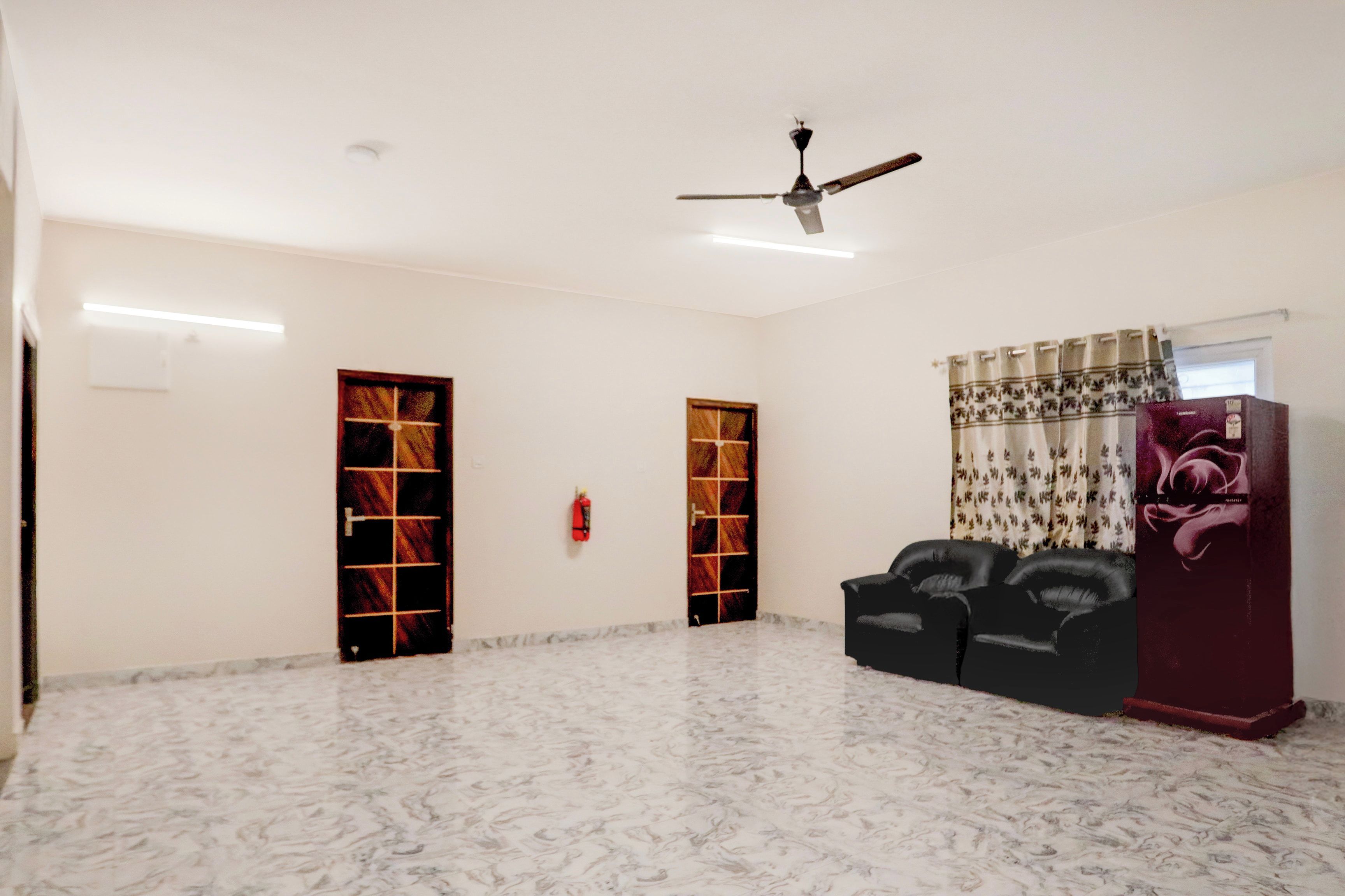 A spacious room with a ceiling fan, two doors, a fire extinguisher, and a sofa.