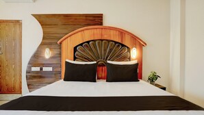 Quarto com cabeceira de madeira, duas almofadas pretas, colcha branca e planta na mesa de cabeceira.