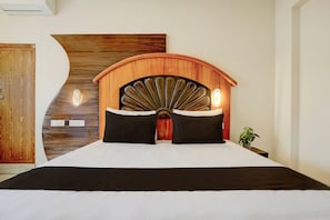 A bedroom with a wooden headboard, two black pillows, a white bedspread, and a bedside plant.