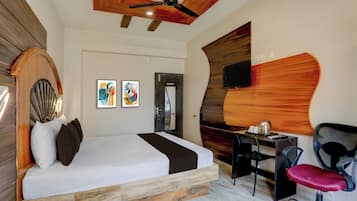 Una habitación de hotel con cama, escritorio, silla, obras de arte y televisor.