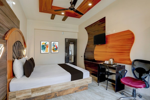 A hotel room with a bed, desk, chair, artwork, and a television.