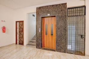 A hotel lobby with a wooden door, a fire extinguisher, and a tiled wall.