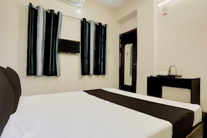 A hotel room with a bed, a flat-screen TV mounted on the wall, a bedside table with a lamp, and a mirror.