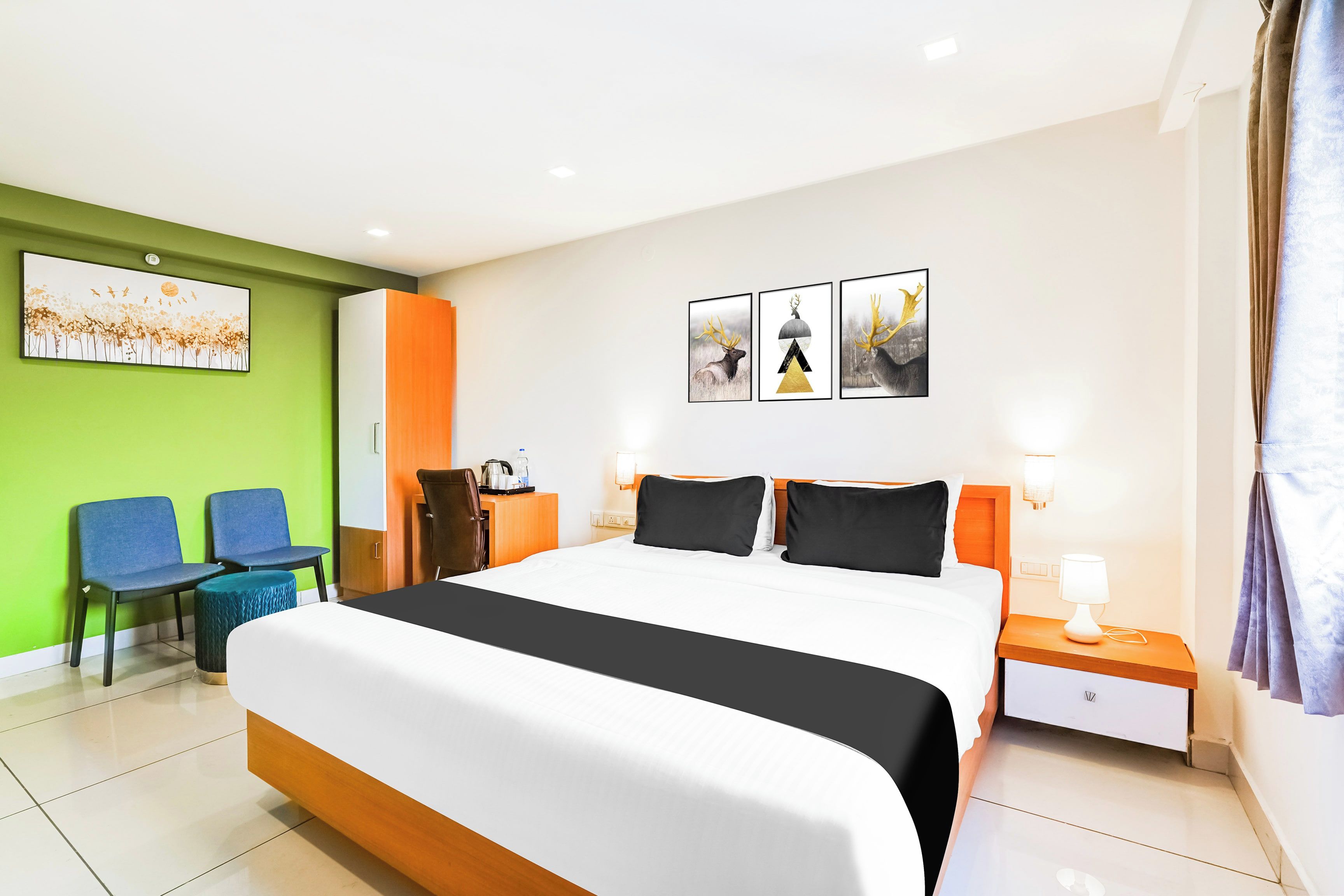 A hotel room with a large bed, a desk, two chairs, a nightstand, and a wall with three framed pictures.