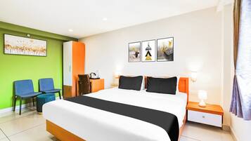 A hotel room with a large bed, a desk, two chairs, a nightstand, and a wall with three framed pictures.