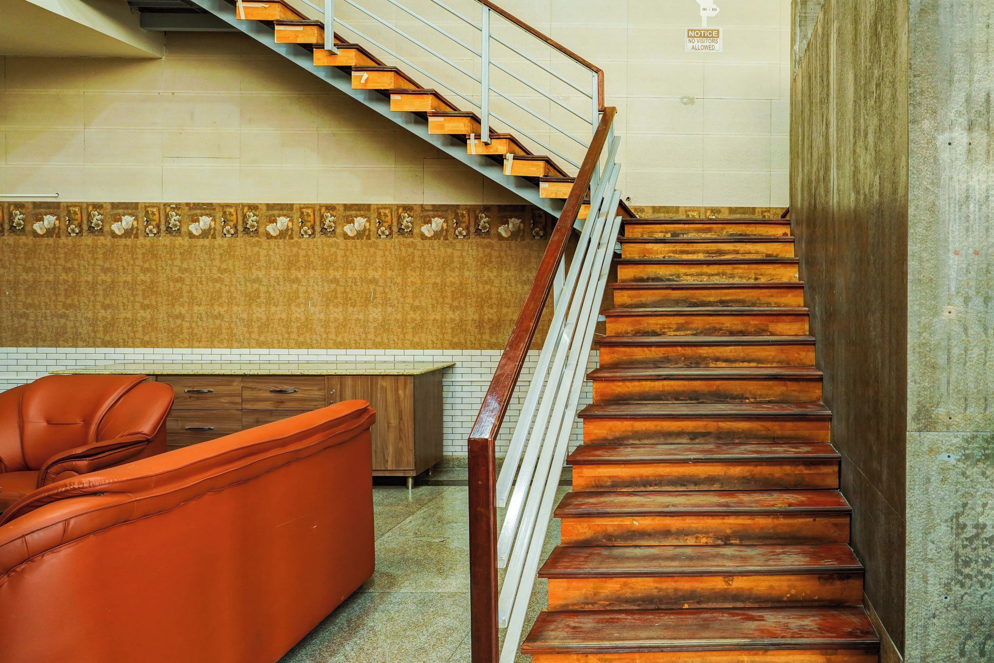 A staircase with wooden steps and metal railings, leading to a landing with a brown leather sofa and a tiled backsplash.