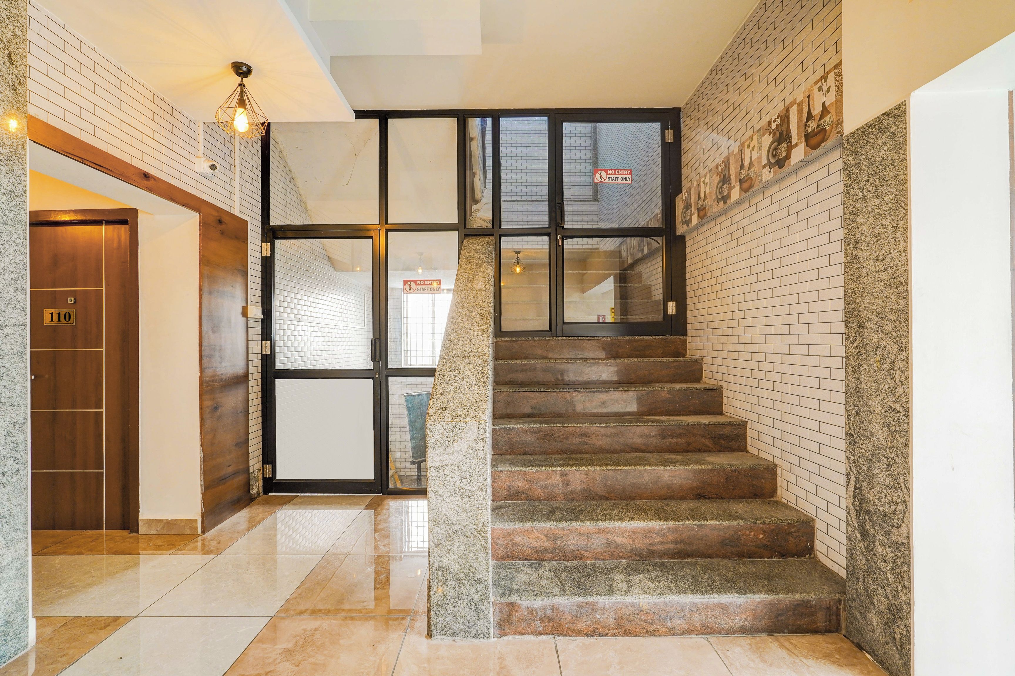 Una escalera con barandilla, una puerta de madera con placa de número y un letrero que indica 'Solo personal, prohibido el acceso'.