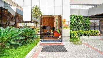 A modern building entrance with a reception desk, seating area, and a view of the surrounding greenery.