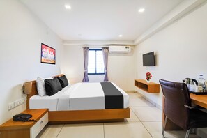 Habitación de hotel con cama, escritorio, silla, aire acondicionado, televisor y ventana con cortinas.