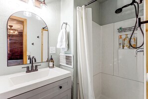 Une salle de bain avec un lavabo blanc, un miroir, une douche avec un rideau et un sèche-cheveux.
