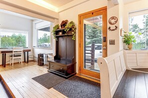 A room with a wooden bench, a fireplace, a dining table with chairs, and a view of the outdoors. - Deck & Views! Family Retreat Near RMNP (Grand Lake)
