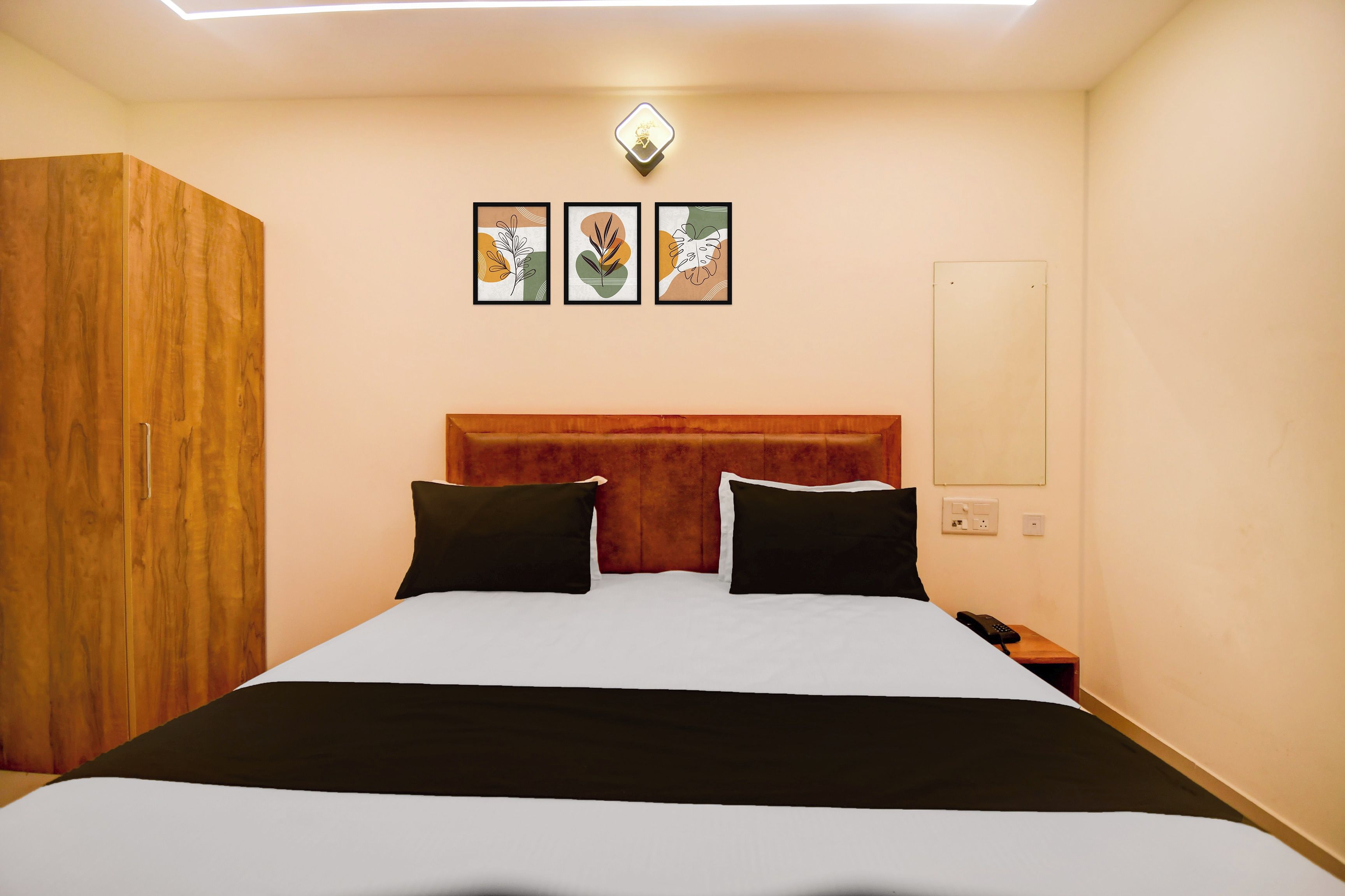 Habitación de hotel con cama, armario de madera, mesita de noche con teléfono y tres cuadros en la pared.