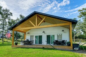 A covered outdoor area with a wooden deck, a dining table with chairs, and a grill. - Lake Ogemaw Escape: Private Beach & Dock (West Branch)