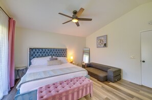 A bedroom with a bed, a ceiling fan, a bedside lamp, a sofa, a bench, and a door. - Indio Paradise: 4-Bedroom Home w/ Resort-Like Pool (Indio)