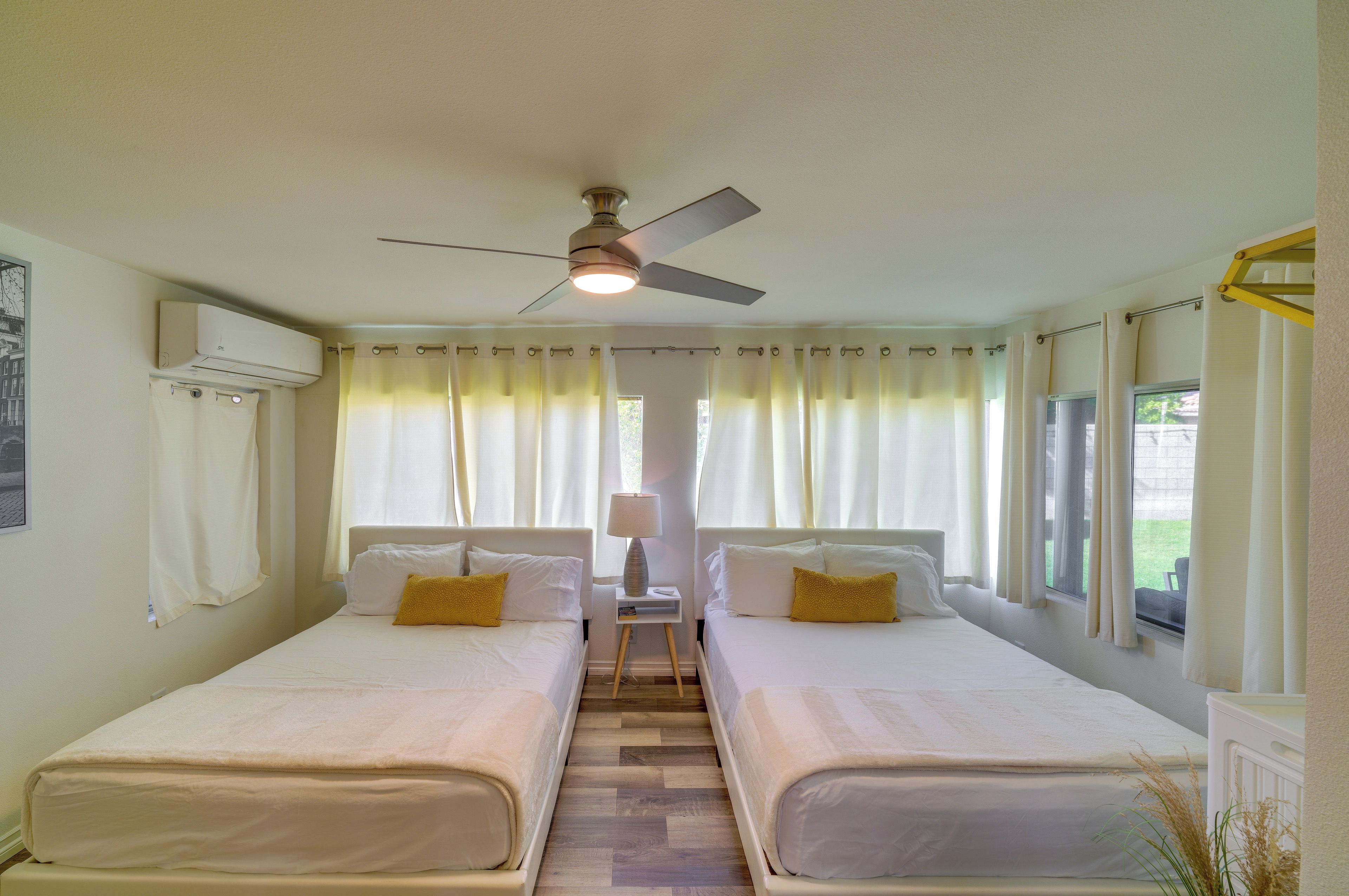 Une chambre d’hôtel avec deux lits, un ventilateur de plafond, une fenêtre avec des rideaux et une table de chevet avec une lampe.