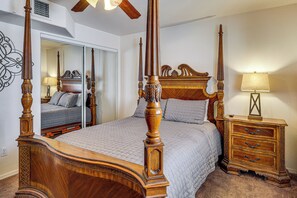 Ein Bett mit Baldachin, ein hölzerner Kopfseitenverkleidung, ein Nachttisch mit Schubladen, ein Spiegel und ein Deckenventilator.