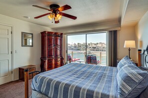 Ein Hotelzimmer mit einem großen Bett, einem hölzernen Schminktisch, einem Deckenventilator, einem großen Fenster mit Blick auf den Strand und einem Balkon mit einem Stuhl.