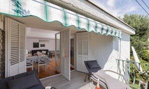 Ein überdachter Außenbereich mit Tisch und Stühlen, einem Fahrrad und einem Balkon mit Geländer.