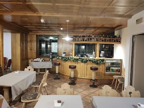 Interior de un restaurante con paneles de madera, zona de bar con taburetes y mesas con sillas.