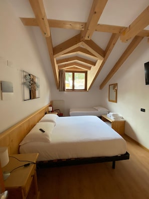 A bedroom with a sloped ceiling, wooden beams, a bed with white linens, a bedside table, a chair, a window with curtains, and a wall-mounted mirror. - Hotel Pizboè (Mazzin)