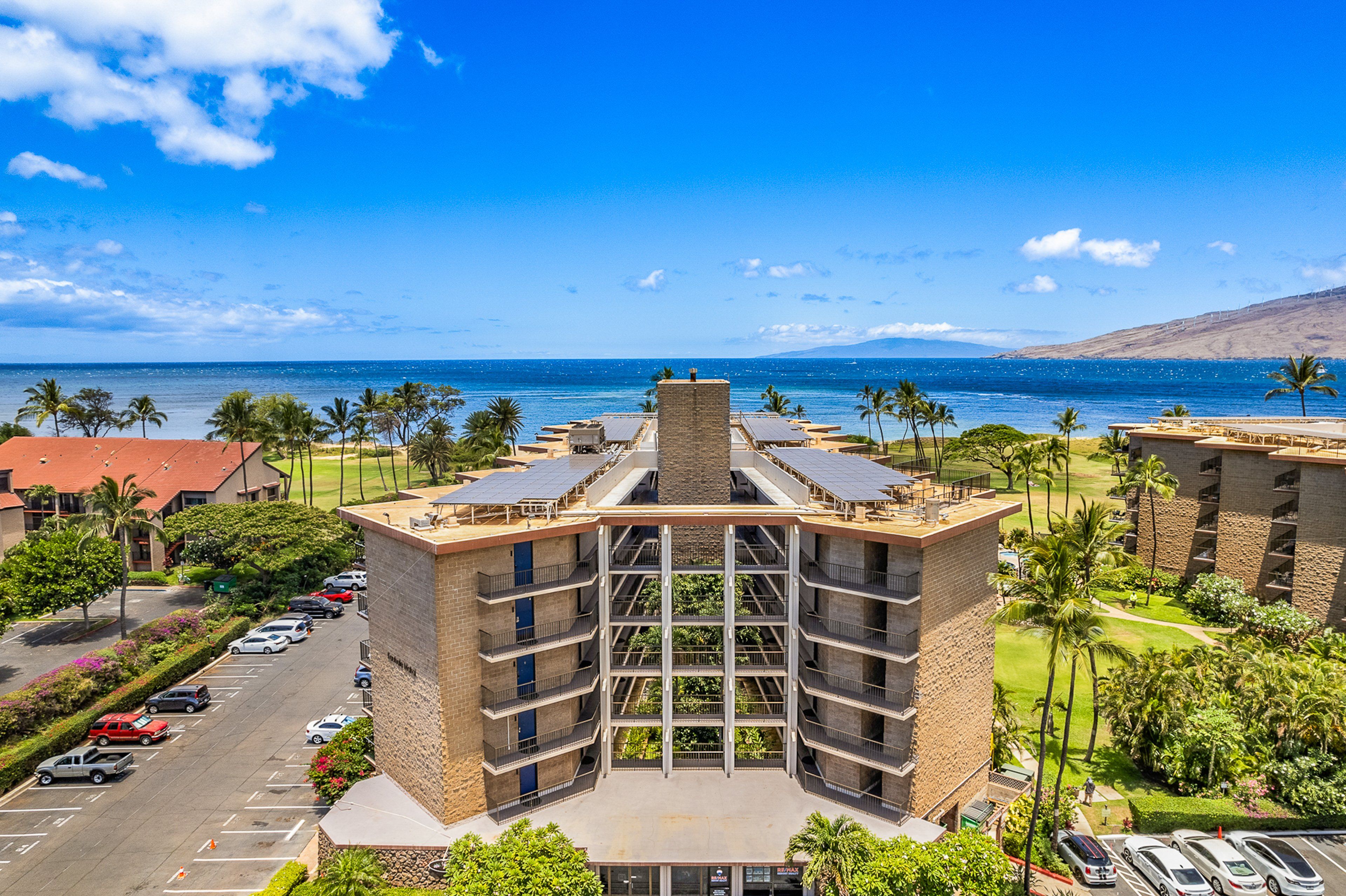 A multi-story hotel with a central courtyard, parking lot, and a view of the ocean.