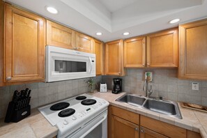 A kitchen with wooden cabinets, a white microwave, a stove, a sink, and a coffee maker. - Ground-Floor 1BD, Garden Views at Oceanfront Resort Sleeps 4-Papakea D105 (Lahaina)