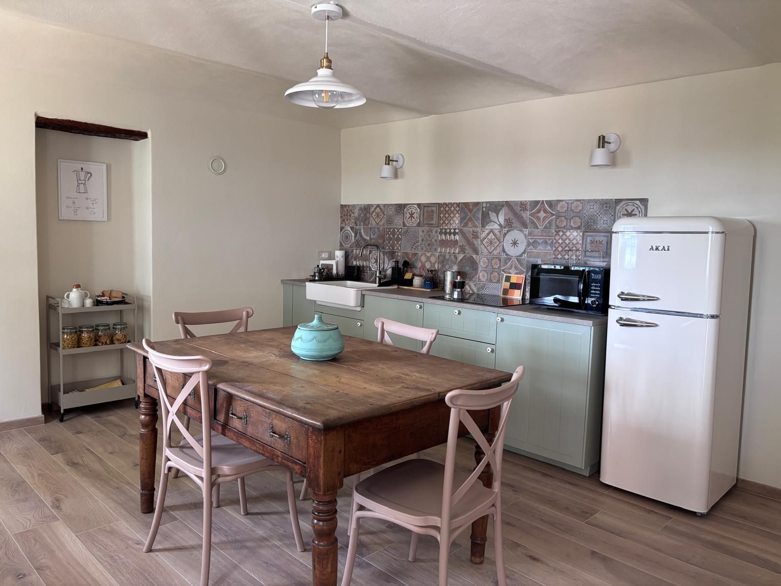 Een kleine keuken met een houten tafel, stoelen, een witte koelkast en een decoratieve achterwand.