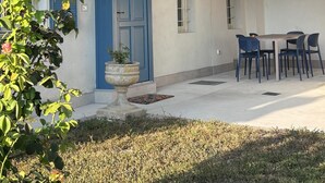 Um edifício de dois andares com varanda, área de refeições com cadeiras e um vaso de planta.