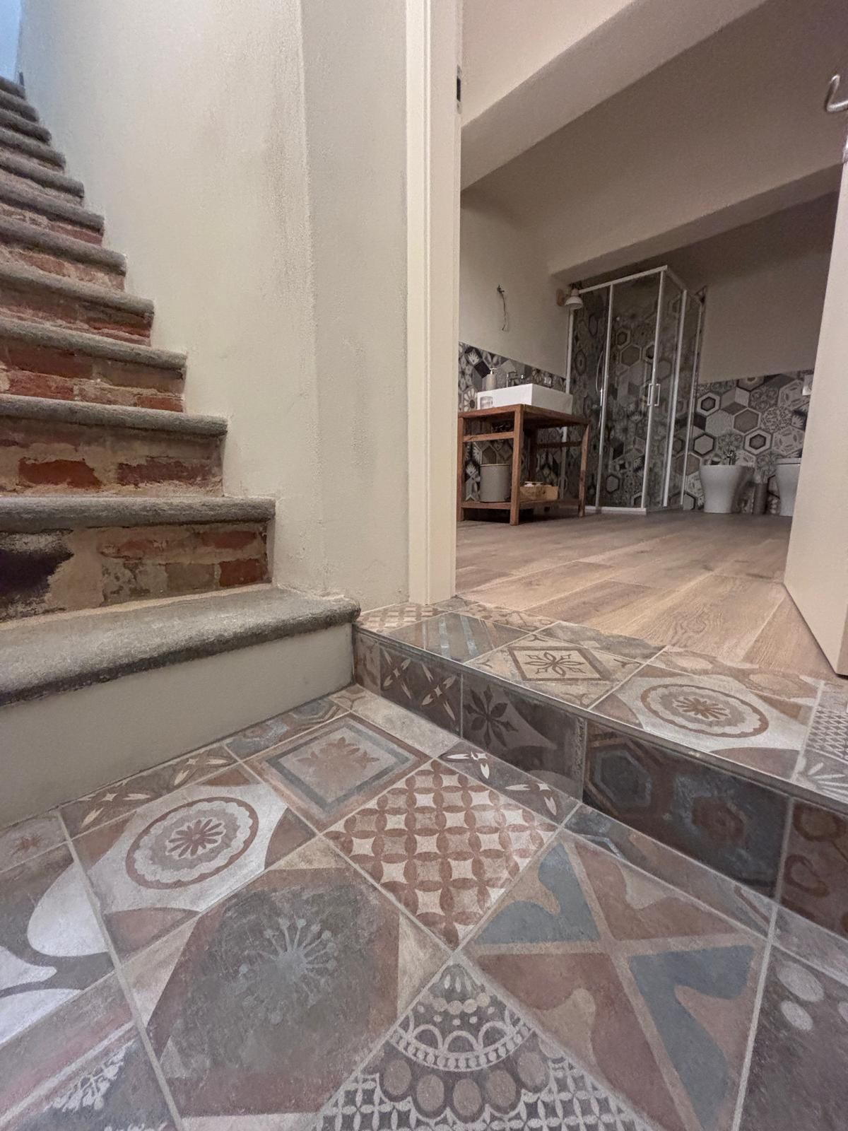 A staircase leading to a room with patterned tiles and a shower area.