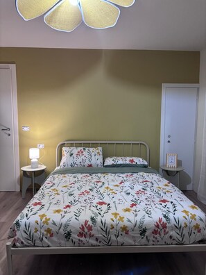 A bedroom with a bed, a bedside table with a lamp, a nightstand, and a door.