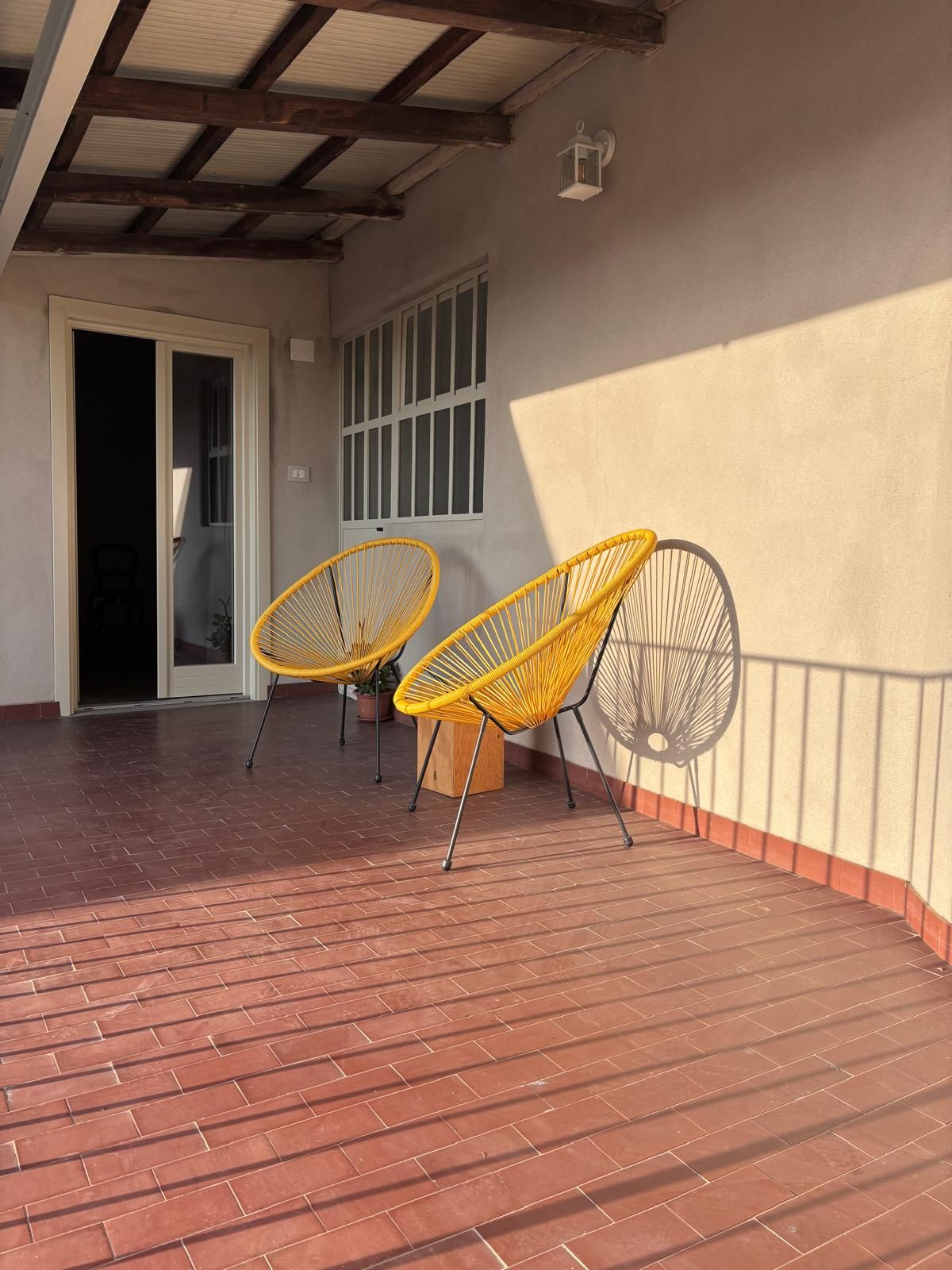 Un'area patio coperta con due poltrone gialle in vimini e una pianta in vaso.