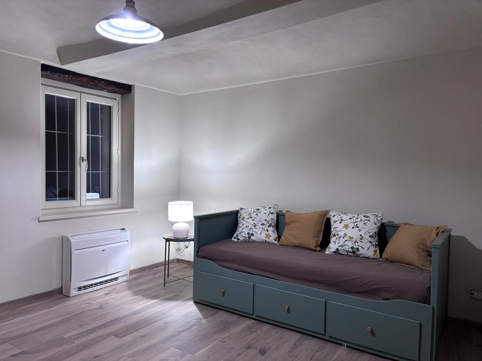 A bedroom with a bed, a window, a heater, and a lamp.
