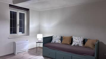 A bedroom with a bed, a window, a heater, and a lamp.