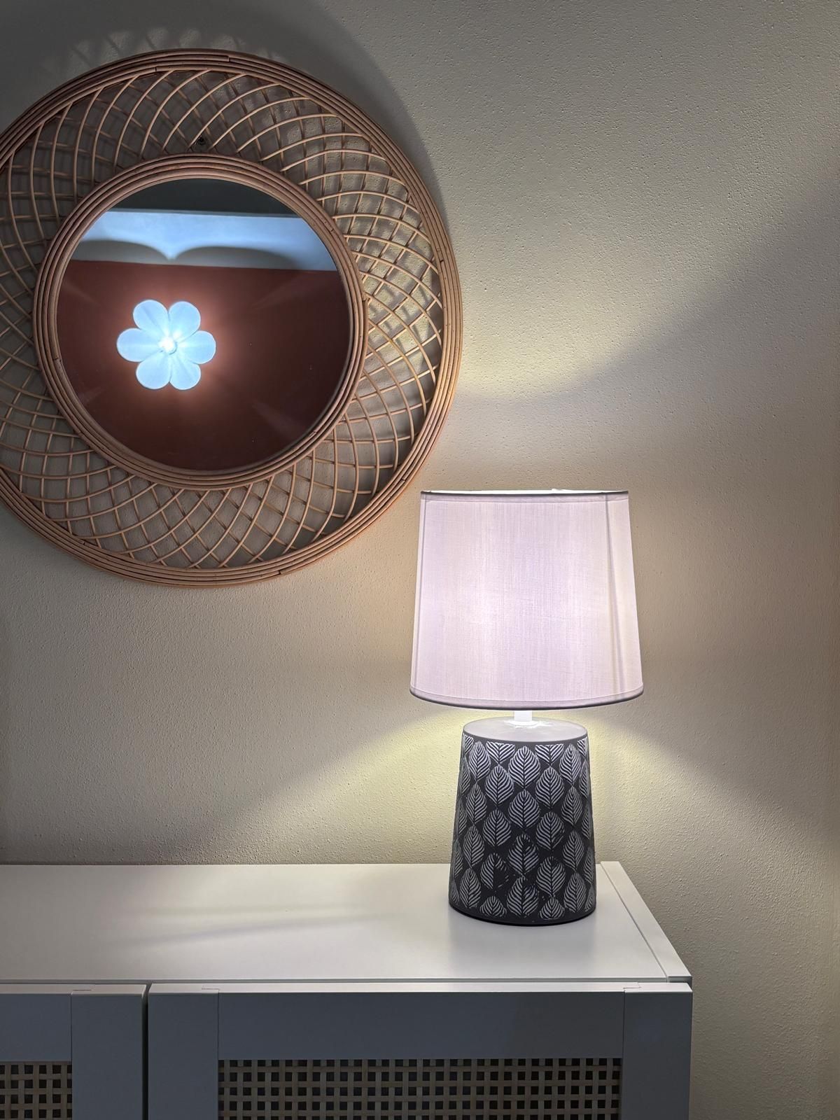 Un miroir mural orné d’un motif géométrique, une lampe au design inspiré des feuilles et une console blanche.