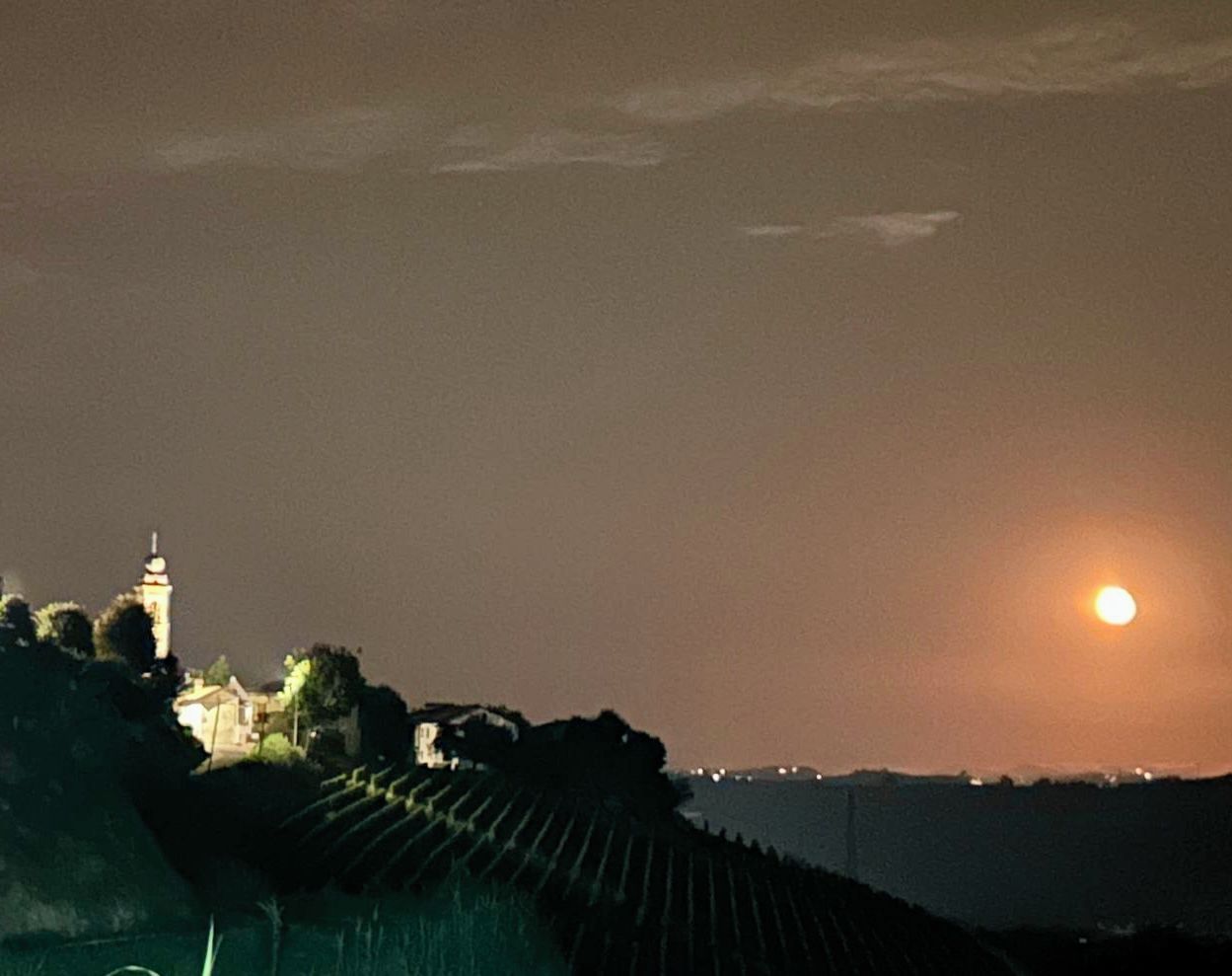 A night scene with a full moon, a tower, and a hillside.