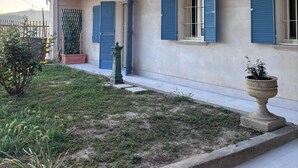 Um edifício de dois andares com varanda, um pequeno jardim e um vaso com planta.
