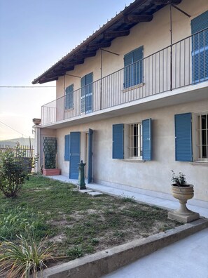 Un edificio su due piani con un balcone, un piccolo giardino e una pianta in vaso.