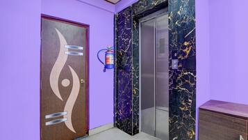 A hallway with a purple wall, a wooden door with a unique design, and an elevator with a marble finish.