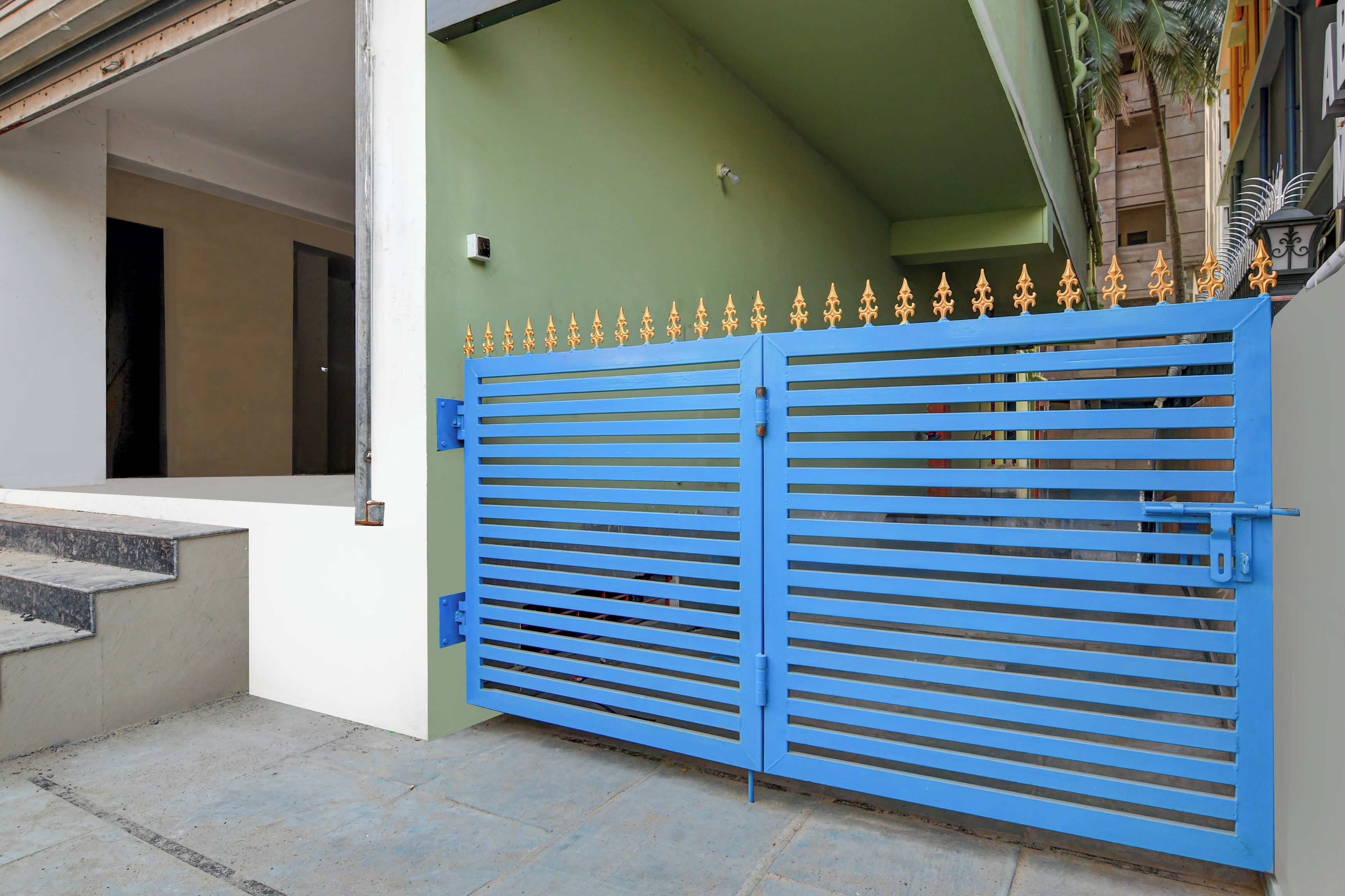 A blue gate with a decorative top, a green wall, and a staircase leading to a building entrance.