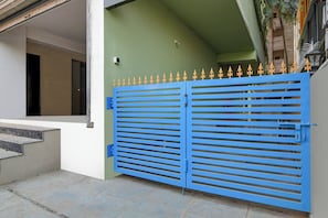A blue gate with a decorative top, a green wall, and a staircase leading to a building entrance. - Townhouse Madhyamgram Chowmatha Bus (Barasat)