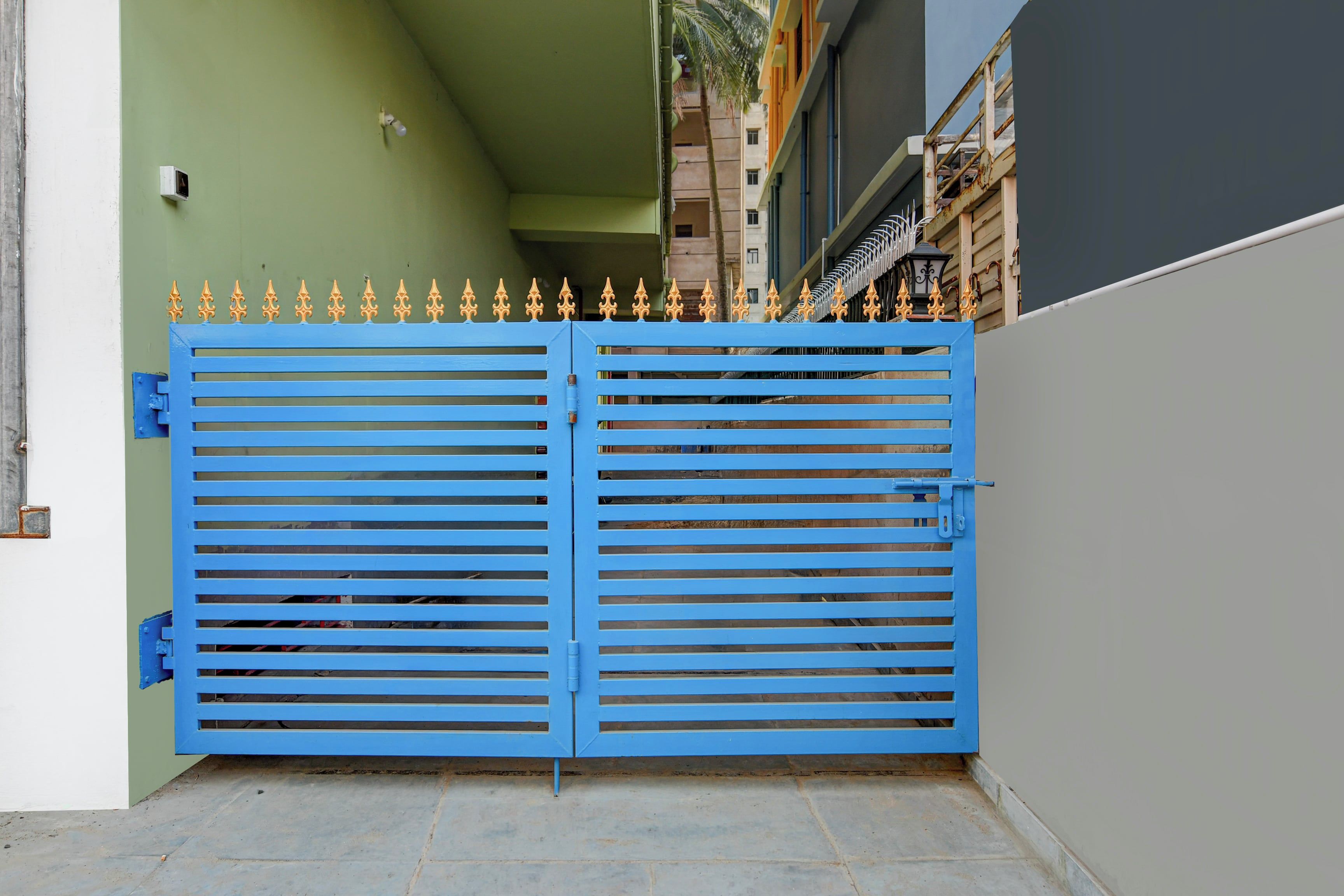 Une porte bleue, ornée d’un motif décoratif en partie supérieure, se dresse devant un bâtiment dont les murs sont respectivement verts et gris.