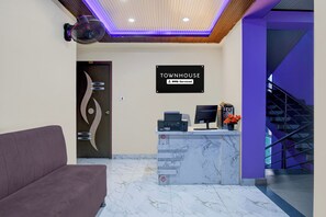 Zona de recepción con un mostrador de mármol, un sofá, un cartel que indica OYO Serviced y una escalera.