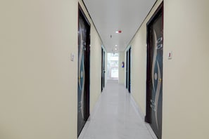 A corridor with doors on both sides, a ceiling with recessed lighting, and a view of the outside through a window at the end. - Townhouse Madhyamgram Chowmatha Bus (Barasat)