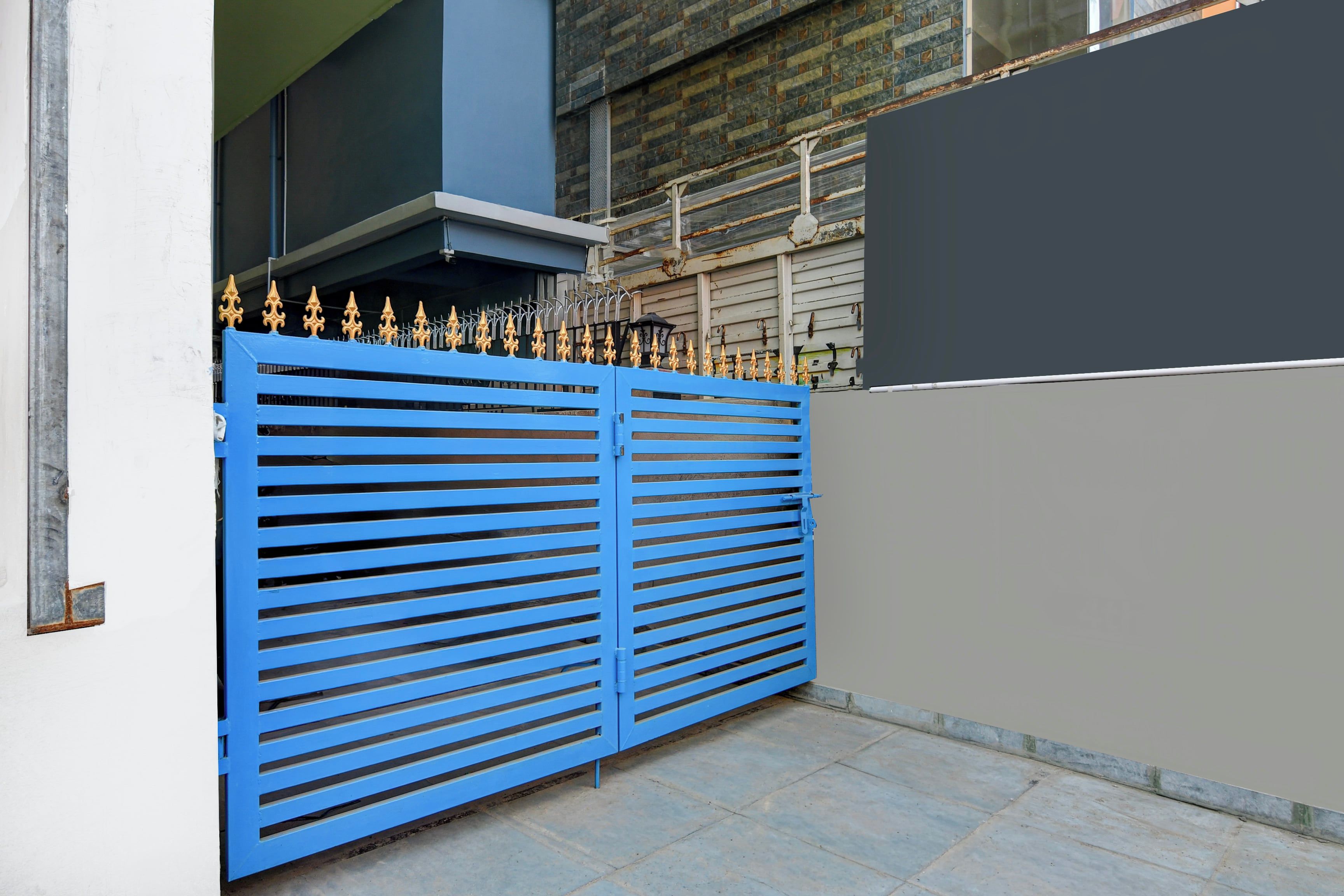 Une porte en métal bleue, ornée d’un motif décoratif en partie supérieure, qui donne accès à un bâtiment à la façade grise et doté d’une cheminée.