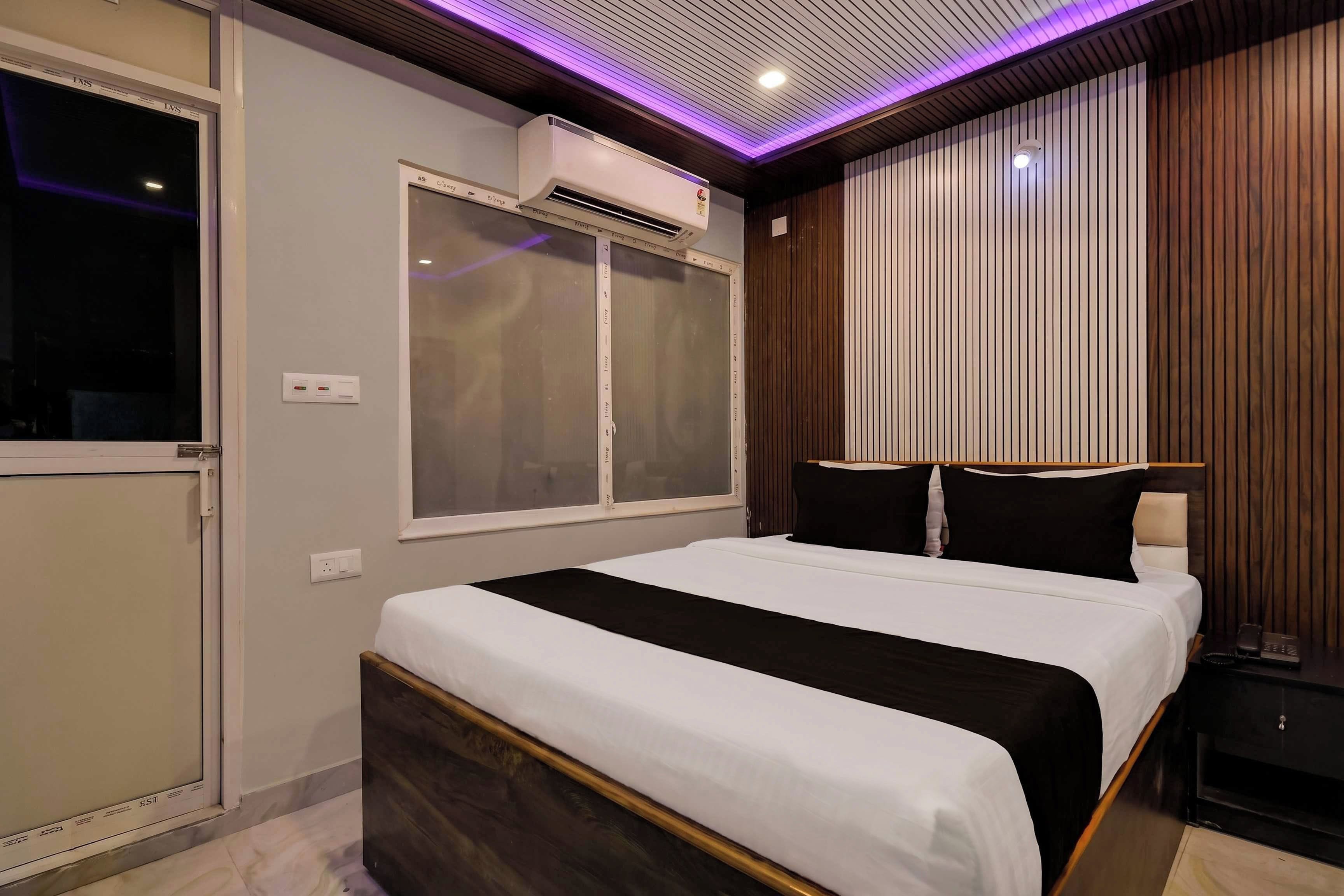 Un dormitorio moderno con una cama, una ventana, un equipo de aire acondicionado y una lámpara fijada a la pared.